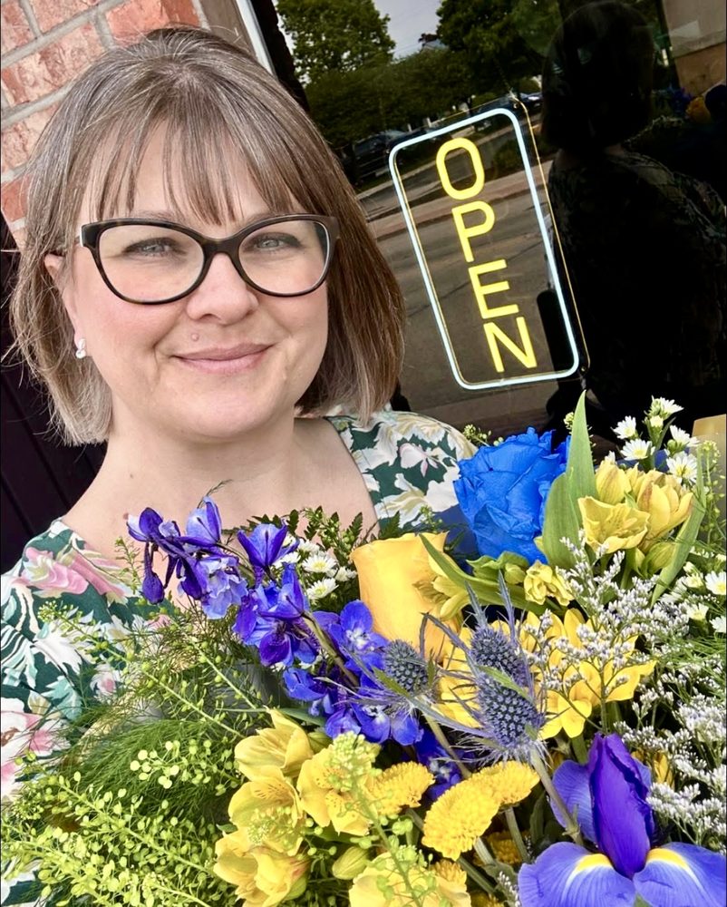 Stephanie, owner of Secret Garden Floral Design, holding an arrangement outside the shop.